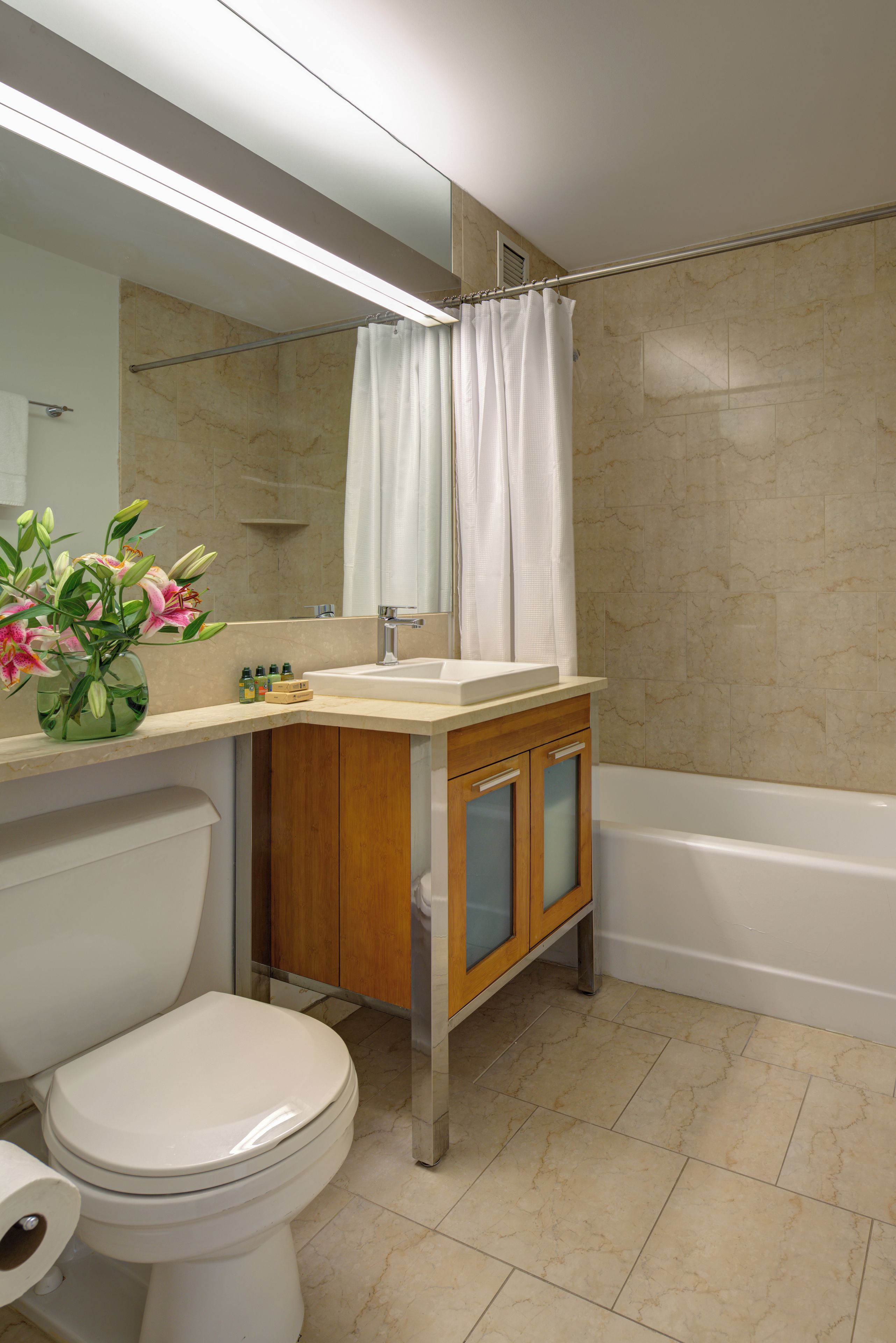 A bathroom with a toilet, sink, mirror, shower curtain, and a vase with flowers.