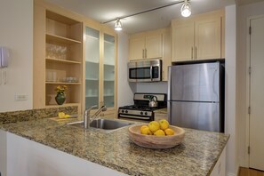 A kitchen with granite countertops, a stainless steel refrigerator, a microwave, a stove, and a bowl of lemons.