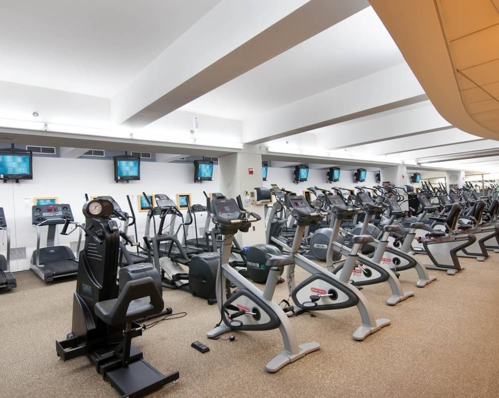 Ein Fitnessstudio mit mehreren Trainingsgeräten, darunter Laufbänder und Ergometer, die in Reihen angeordnet sind.