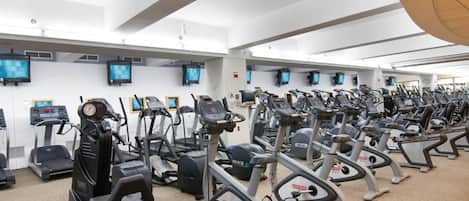 A gym with multiple exercise machines, including treadmills and stationary bikes, arranged in rows.
