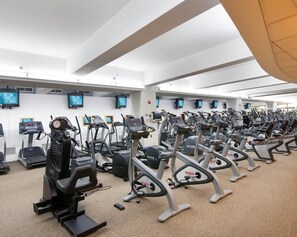 A gym with multiple exercise machines, including treadmills and stationary bikes, arranged in rows.
