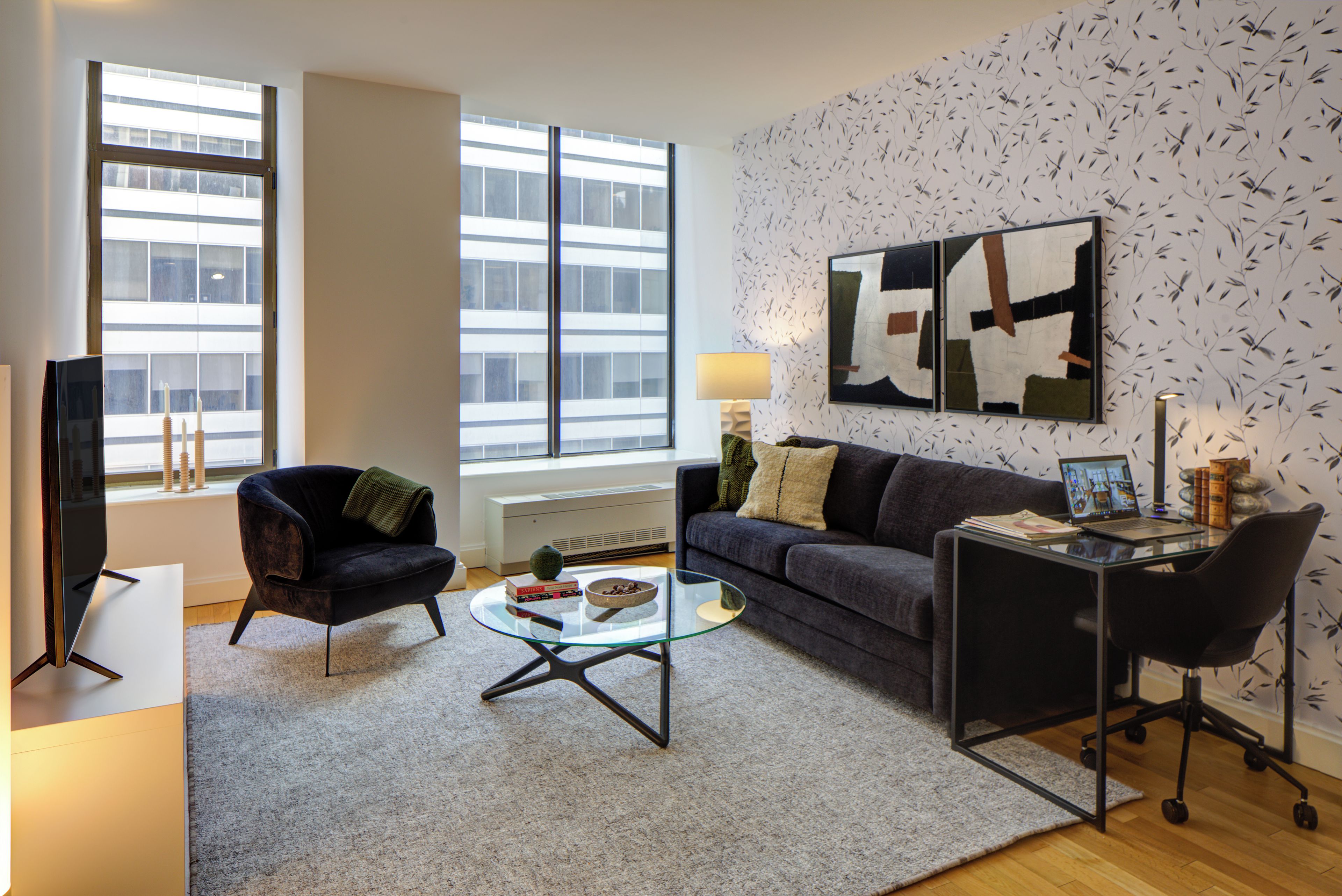 A modern living room with a sofa, armchair, glass coffee table, and a desk with a chair.