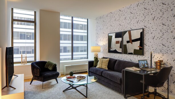 Una sala moderna con sofá, sillón, mesa de centro de vidrio y un escritorio con silla.