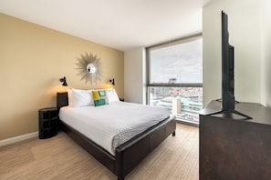 A modern hotel room with a large bed, a city view, a flat-screen TV, and a unique wall decoration.