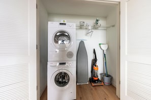 A laundry area with stacked washing machines and an ironing board.