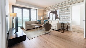 A modern living room with a sofa, armchair, and coffee table, a dining area with a table and chairs, and a large window with blinds. - Boston 2 Bedroom, Across from Fenway Park (Boston)