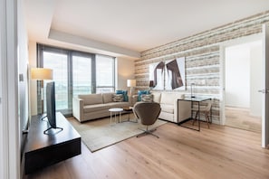 A modern living room with a sofa, armchair, and coffee table, a dining area with a table and chairs, and a large window with blinds.
