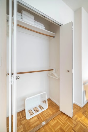 Et walk-in closet med trægulv, en bøjlestang og en hvid kurv.