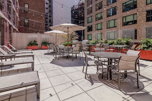 An outdoor patio with tables and chairs, surrounded by brick buildings and greenery. - Brooklyn Heights Living | Doorman, On-Site W/D (Brooklyn)