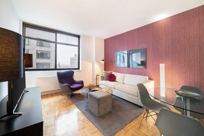 A modern living room with a sofa, armchair, ottoman, and glass table. - Brooklyn Heights Living | Doorman, On-Site W/D (Brooklyn)