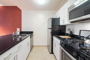 A modern kitchen with a black stove, stainless steel appliances, and white cabinetry. - Brooklyn Heights Living | Doorman, On-Site W/D (Brooklyn)