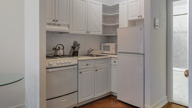Una cocina compacta con armarios blancos, estufa, microondas y refrigerador.