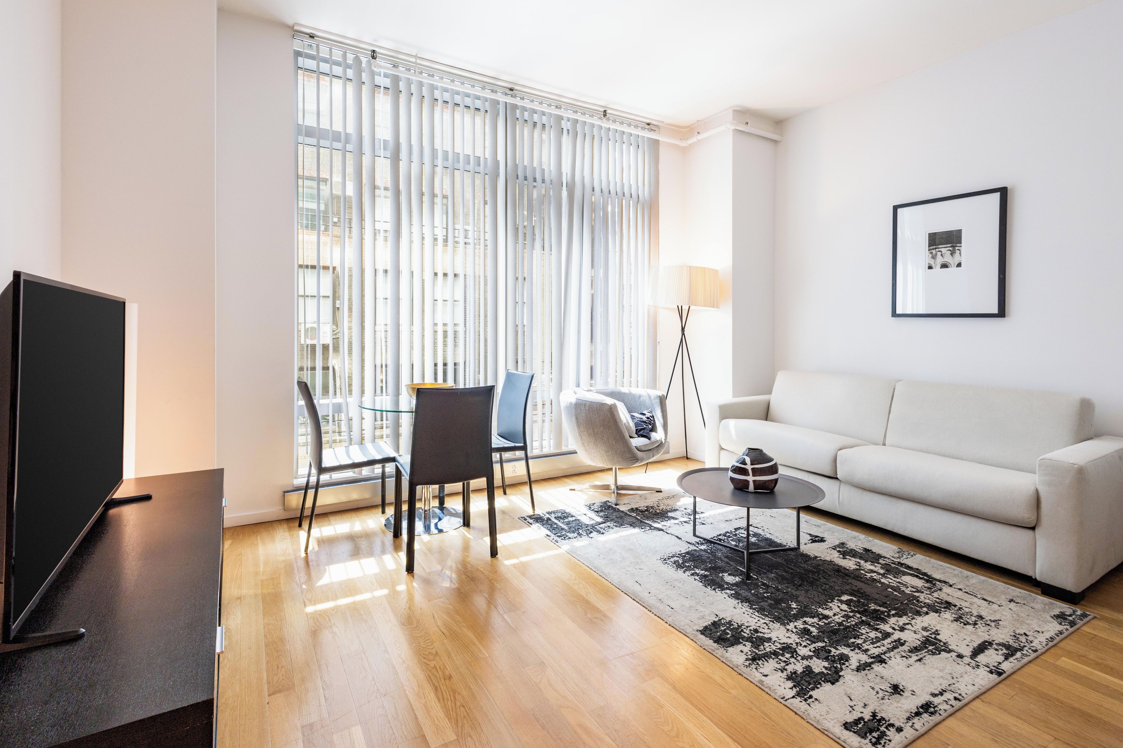 Un salon moderne avec un téléviseur à écran plat, un canapé blanc, une table basse et un tapis à motifs.