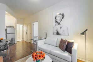 Een moderne woonkamer met een witte bank, een glazen salontafel met bloemen, een zwarte vloerlamp en een groot zwart-wit portret aan de muur.