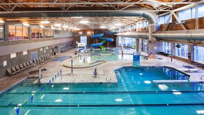 An indoor swimming pool with multiple lanes, a water slide, and seating areas.