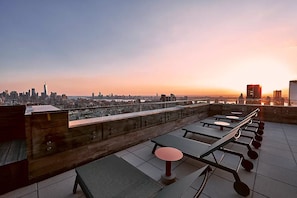 A rooftop terrace with tables and chairs, offering a city skyline view.