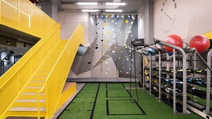 Una pared de escalar con agarraderas, una escalera amarilla y un estante con pelotas de ejercicio.