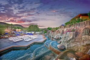 A resort pool area with lounge chairs and umbrellas, surrounded by rocky terrain and a sunset sky. - Water Oasis + Golf Course + Spa! 1 Bedroom Suite. (Phoenix)