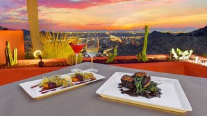 A table with two plates of food and two glasses of wine, set against a sunset view. - Water Oasis + Golf Course + Spa! 1 Bedroom Suite. (Phoenix)