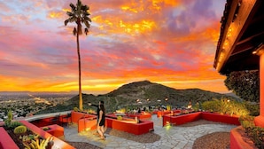 Une terrasse sur le toit agrémentée de jardinières rouges, d’un palmier et offrant une vue sur une chaîne de montagnes au coucher du soleil.