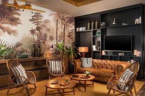 A living room with a sofa, two armchairs, a coffee table, a TV, and a bookshelf. - Nh Lyon Aeroport (Colombier-Saugnieu)