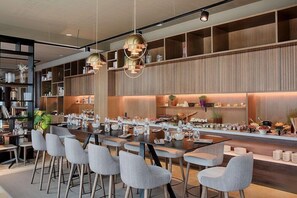 A modern dining area with a long table, multiple chairs, and pendant lighting. - Nh Lyon Aeroport (Colombier-Saugnieu)