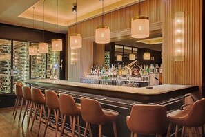A bar area with a counter, stools, and hanging lights. - Nh Lyon Aeroport (Colombier-Saugnieu)