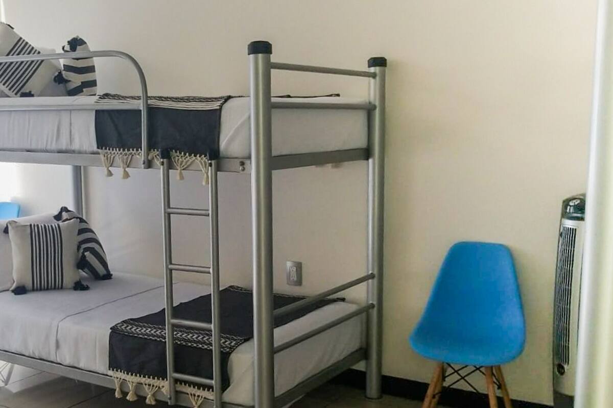 A bunk bed with a ladder, pillows, and a blanket. There is a blue chair and a heater in the room.