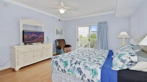 A bedroom with a bed, a dresser, a television, a chair, a balcony with a view, and a ceiling fan. - ⭐️Astoria 207 Ocean/Bayside Views Rooftop Pool Linens⭐️ (Ocean City)