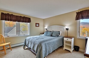 Une chambre à coucher avec un lit, deux tables de chevet, une chaise et une fenêtre avec des rideaux.
