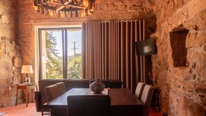 A stone-walled room with a large window, a dining table with chairs, a television, and a lamp. - Buganvília Loft - Quinta do Tapadinho (Cabeceiras de Basto)
