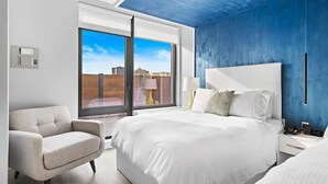 Une chambre d’hôtel moderne dotée d’un grand lit, d’un canapé, d’une table de chevet et offrant une vue sur la ville grâce à une grande fenêtre.