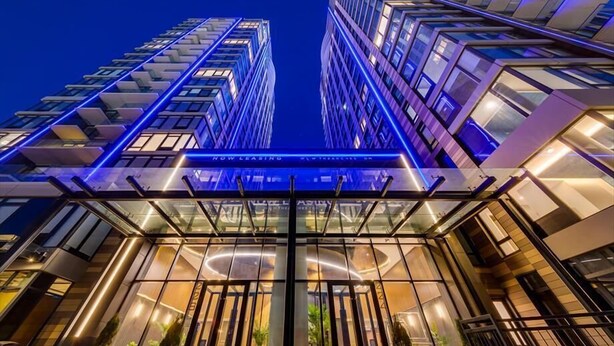 Een modern hotel met een glazen gevel, meerdere verdiepingen en een opvallend bord met de tekst 'NU TE HUUR'.
