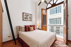 A bedroom with a bed, a nightstand, a framed picture, a window with shutters, and a balcony with a railing. - Historic 2BR: Walk Everywhere • King Bed • Balconies with Views (San Juan)