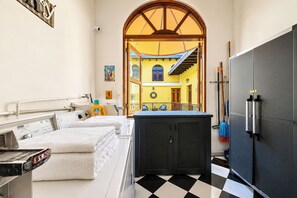 Habitación de hotel con piso de cuadros, cama con sábanas blancas, un mueble negro grande y vista al interior por un arco.