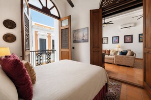 Un dormitorio con cama, balcón, vista de un edificio, sofá y un cuadro en la pared.