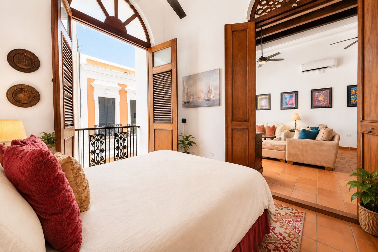 A bedroom with a bed, a balcony, a living area with a sofa, and a dining table.