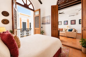 A bedroom with a bed, a balcony, a living area with a sofa, and a dining table.