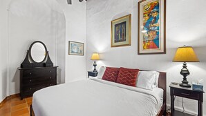 Ein Schlafzimmer mit einem Bett, einem Schminktisch, zwei Nachttischen mit Lampen und zwei gerahmten Bildern an der Wand.