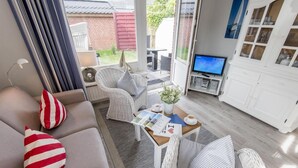 Uma sala de estar moderna com um sofá, almofadas listradas, uma poltrona de vime, uma mesa de centro com revistas e uma televisão.