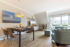 A modern loft apartment with a dining area, a living room, and a large window offering a view of the outdoors.