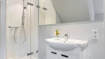 A modern bathroom with a glass-enclosed shower, a white sink with a vase of flowers, and a mirror above the sink.