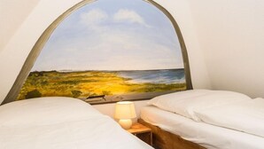 Et soveværelse med to senge, et natbord med lampe, og et stort landskabsmaleri på væggen.