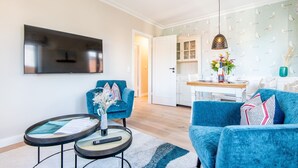 Un salon équipé d’un téléviseur à écran plat, d’un canapé bleu, d’un fauteuil bleu, d’une petite table ronde avec une télécommande et d’une suspension.