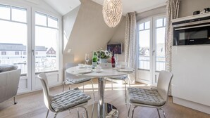 Een moderne eethoek met een ronde tafel, twee gestoffeerde stoelen, een kroonluchter en uitzicht op buiten.