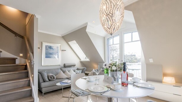 Een moderne loft-woonkamer met een eethoek, voorzien van een trap, een zithoek, een kroonluchter en een groot raam met uitzicht.