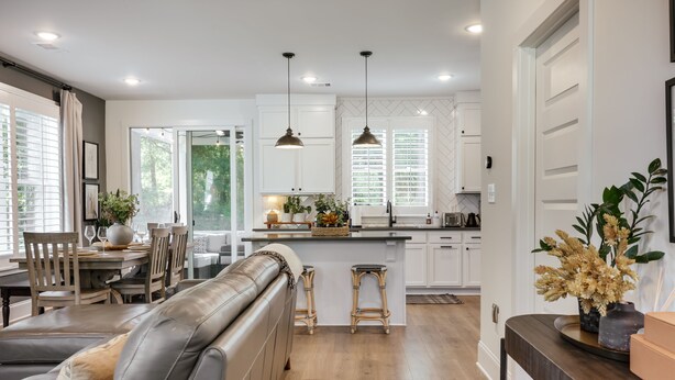 Une cuisine moderne avec des meubles blancs, un îlot central, des luminaires suspendus et un coin repas comprenant un canapé en cuir et des chaises en bois.