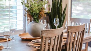Une table de salle à manger en bois, des chaises, un vase avec des fleurs et des verres à vin.