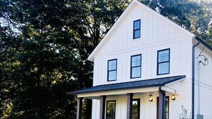 Une maison blanche à deux étages, dotée d’un porche et d’un petit jardin.