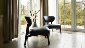 A room with a large window, a black chair, a black ottoman, and a vase with flowers. - Bungalowpark It Wiid by Interhome (Eernewoude)